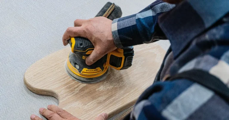 carpenter sanding a wood board with a power sander before repairing the surface