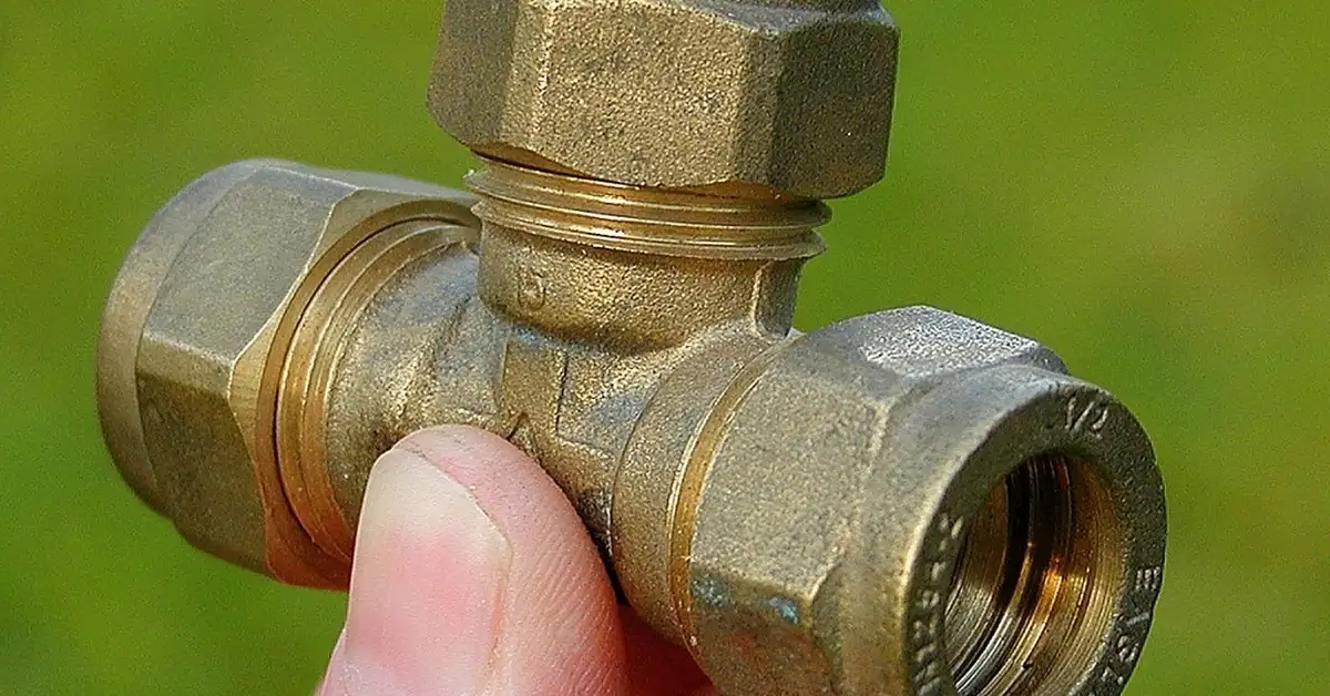 Hand holding a brass compression fitting used to transition PVC pipe to copper pipe