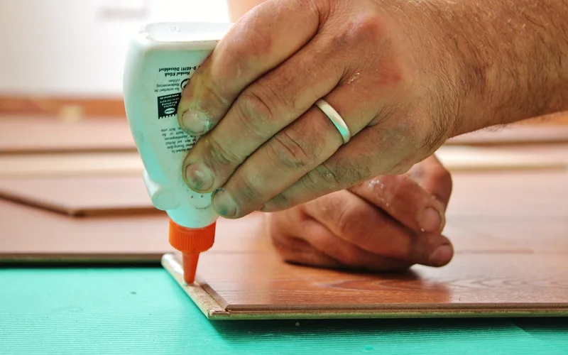 hand applying wood glue from a bottle to a tongue-and-groove flooring joint