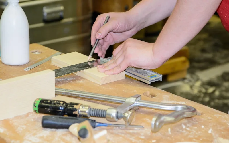 wood glue bottle next to a clamp and measuring tools on a carpentry workbench