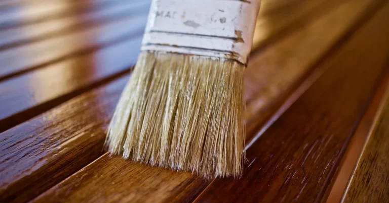 brush applying a wet glossy topcoat to a reddish stained wood surface