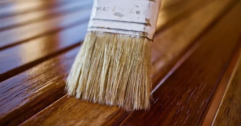 Paintbrush applying stain to dry pressure-treated wood deck boards