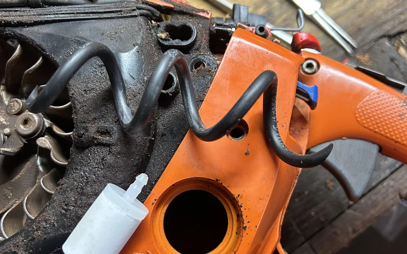 close-up of a chainsaw carburetor and fuel tank grommet with the fuel line disconnected for replacement close-up of a chainsaw carburetor and fuel tank grommet with the fuel line disconnected for replacement
