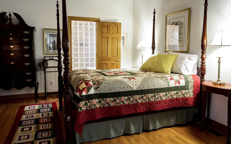 Woven rug runner lying flat on a hardwood bedroom floor beside a four-poster bed