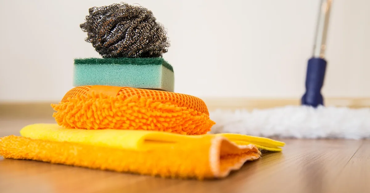 cleaning cloths, scrub sponge, and mop laid out on a hardwood floor for wax removal