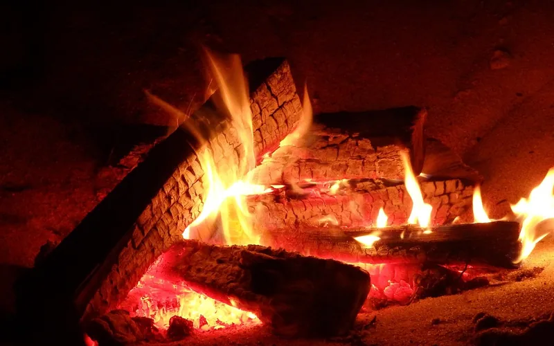 Wood logs burning with visible flame during combustion, releasing heat and light