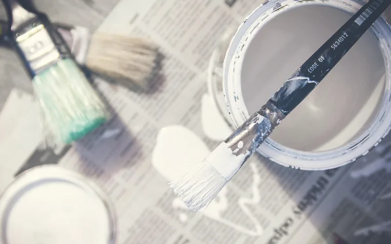 Open cans of white paint with brushes resting on a drop cloth during a home renovation