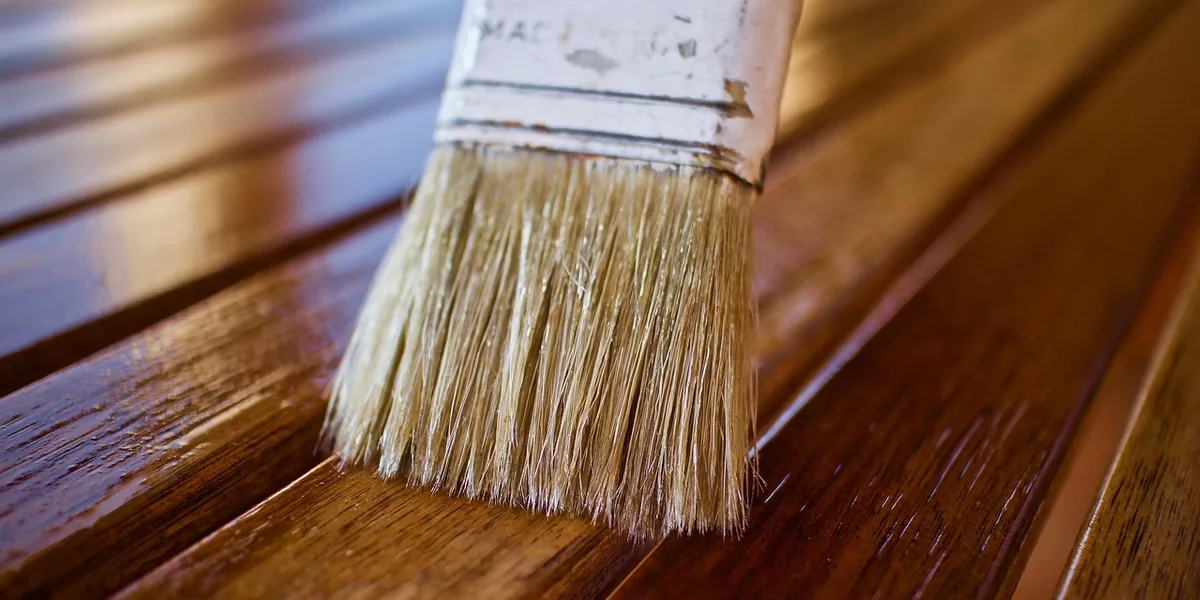 close-up of a paintbrush applying glossy oil-based polyurethane to a wood surface