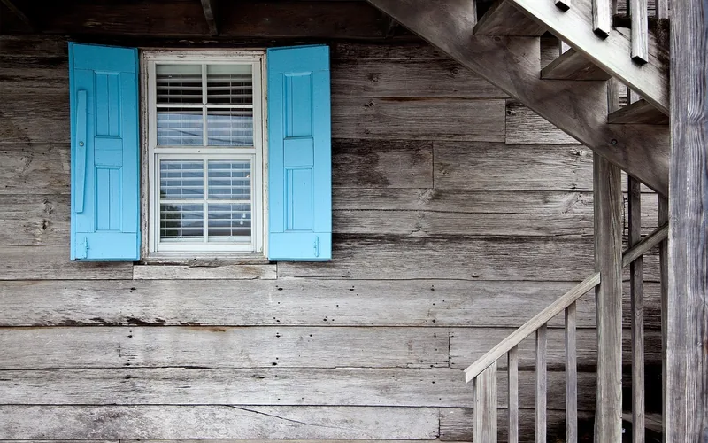 Turquoise-blue painted shutters framing a window against weathered gray wood siding