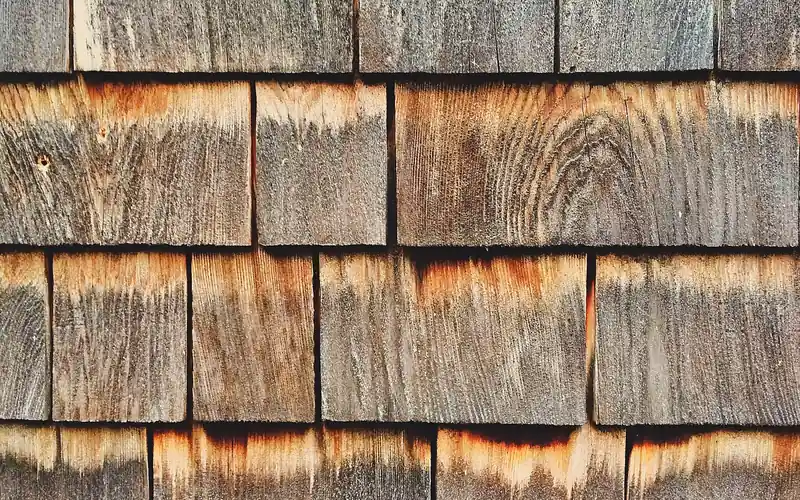 Weathered cedar shingles fading from reddish-brown to silver-gray after years of UV exposure