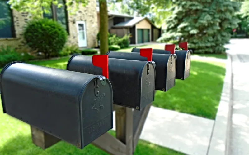 row of black post-mounted mailboxes with red flags up on a suburban street