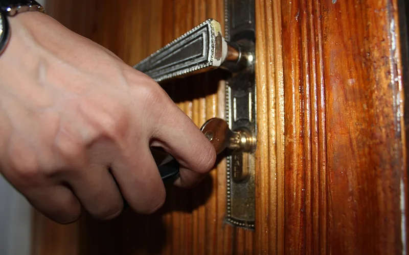 hand inserting a slim metal pick into a brass door lock cylinder