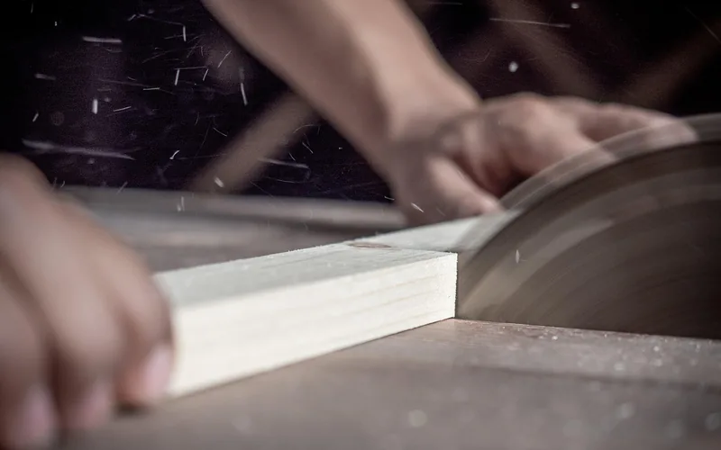 Carpenter's hands guiding a wood plank through a table saw