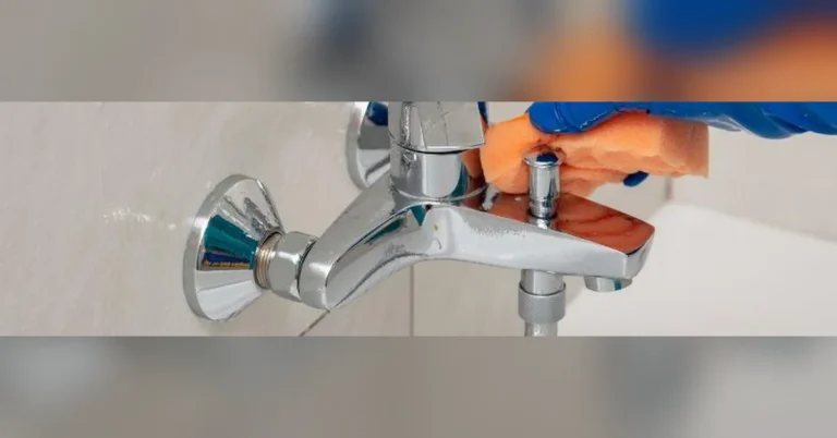 Gloved hand scrubbing a brushed nickel bathroom faucet with an orange sponge