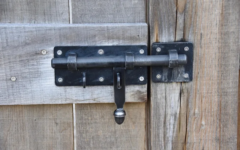 black slide bolt lock mounted on a wood door frame, a footbolt-style locking mechanism