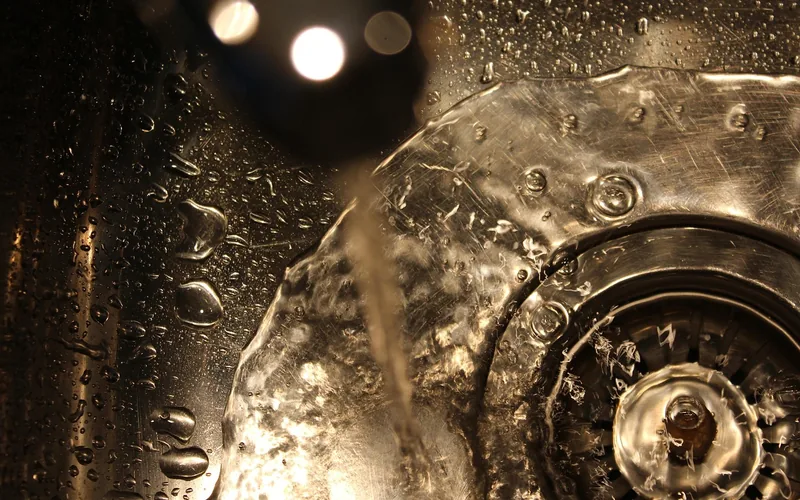 water draining from a stainless steel bathroom sink basin after a clog is cleared