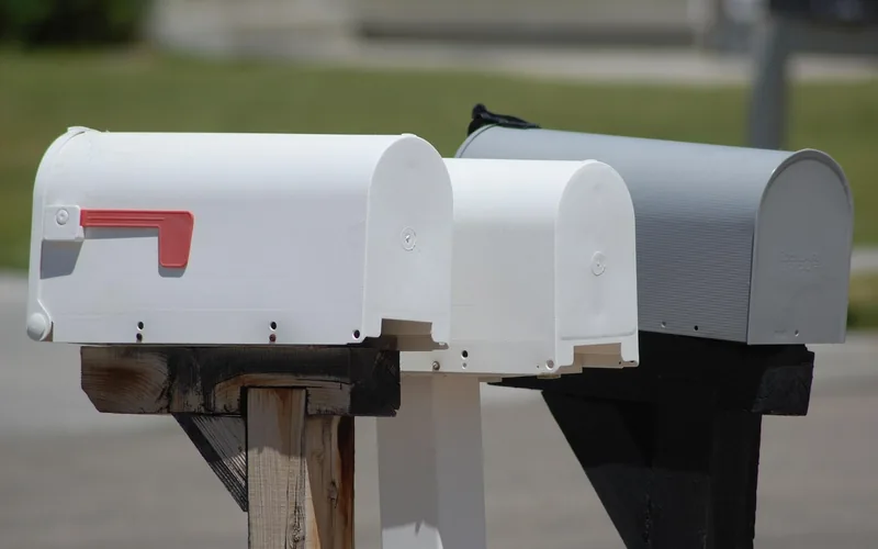 three white and gray post-mounted mailboxes lined up on wooden posts