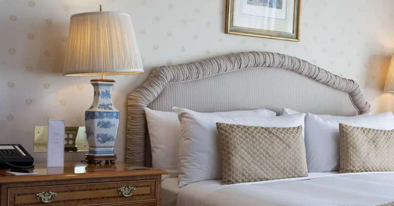 White and blue ceramic table lamp glowing on a wood nightstand beside an upholstered bed