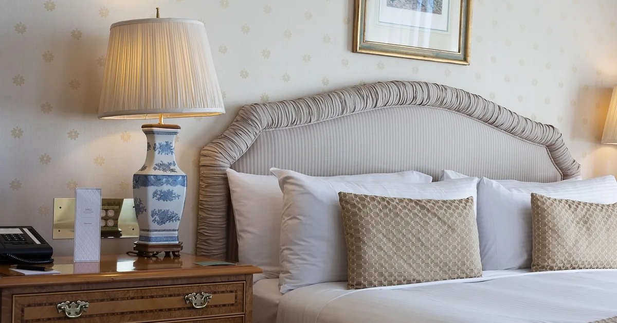 White and blue ceramic table lamp glowing on a wood nightstand beside an upholstered bed