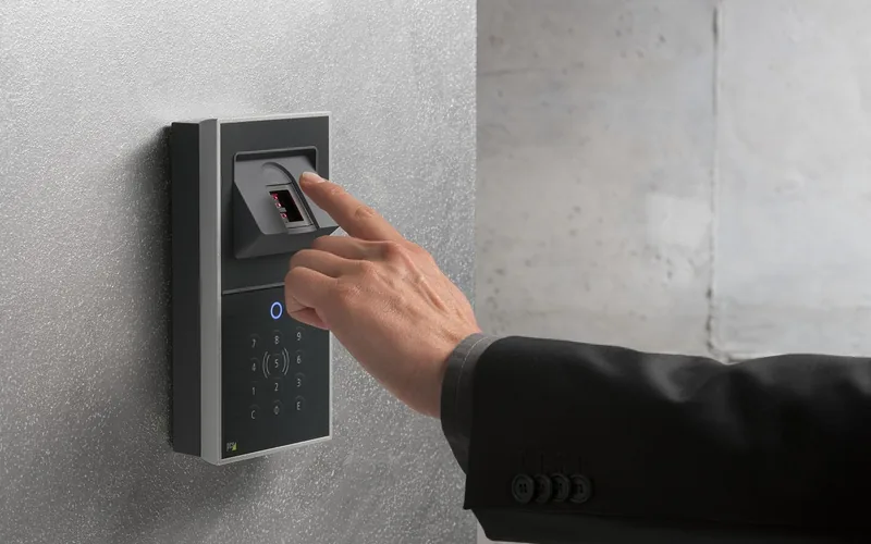 Person using a fingerprint biometric scanner on a wall-mounted access control panel