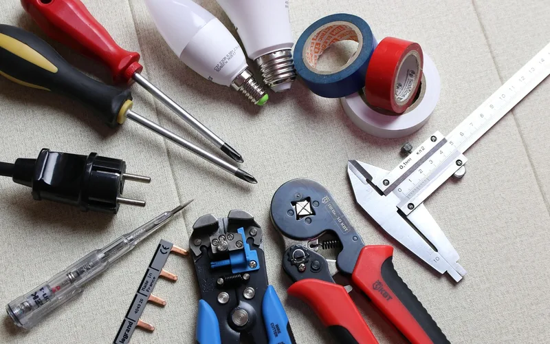 Screwdrivers, wire strippers, a voltage tester, and electrical tape laid out before a flush mount light install