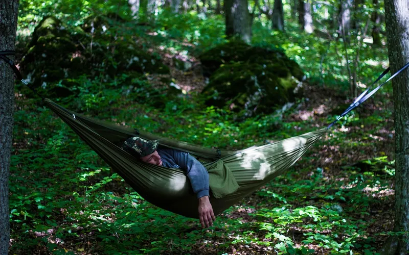 Camper resting in a hammock under a tarp shelter strung between trees in a forest Camper resting in a hammock under a tarp shelter strung between trees in a forest
