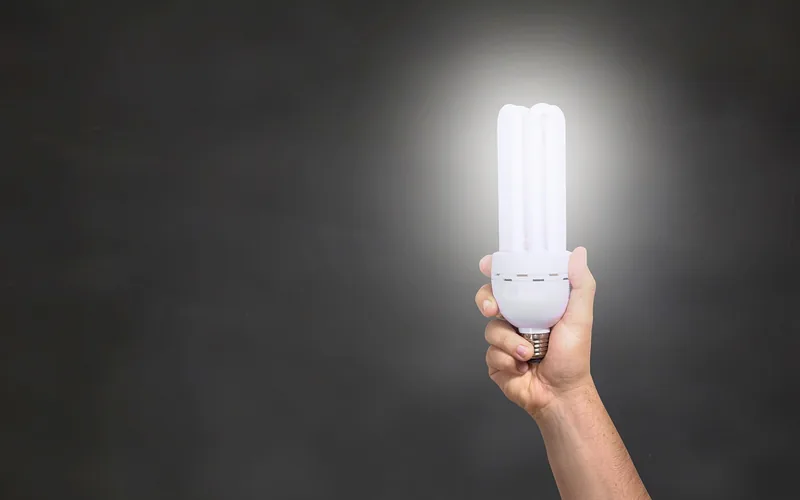 hand holding a lit CFL replacement bulb, one bulb type compatible with ceiling fan light kits