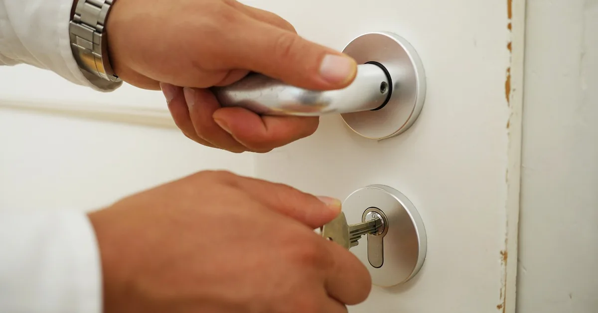 Hand inserting a key into a door lock cylinder next to the door handle