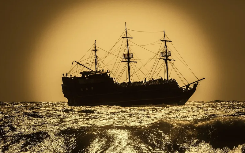 pirate-style sailing ship silhouette crossing open water at sunset pirate-style sailing ship silhouette crossing open water at sunset