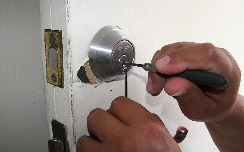 locksmith's hands using a pick tool on a deadbolt lock cylinder, since deadbolts cannot be opened with a card locksmith's hands using a pick tool on a deadbolt lock cylinder, since deadbolts cannot be opened with a card