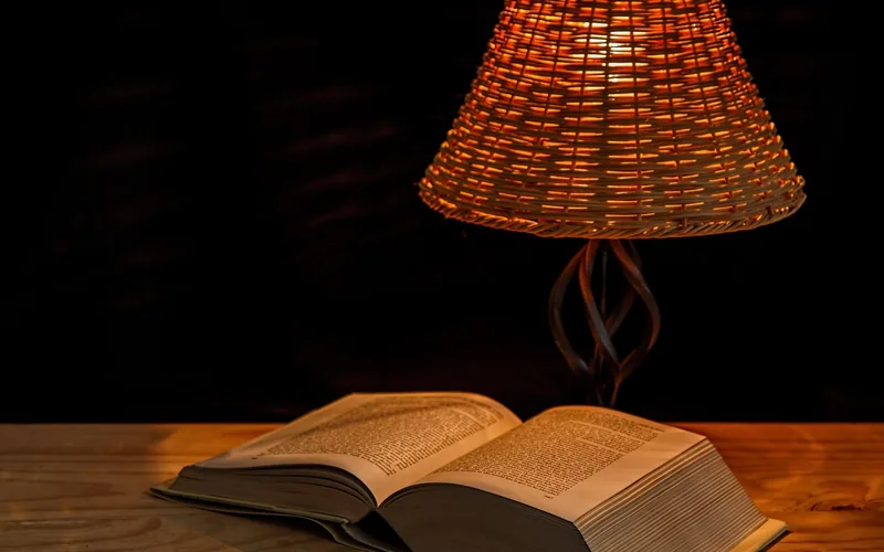 Close-up of a woven empire-style lamp shade lit above an open book