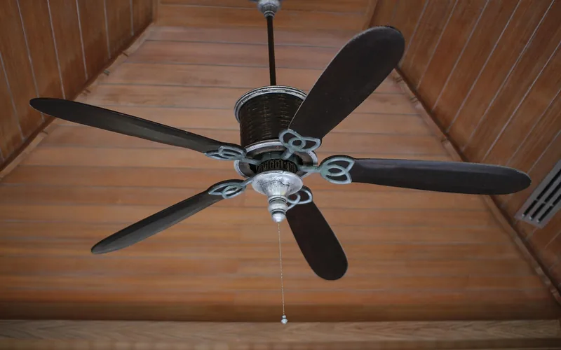 five-blade decorative ceiling fan with a pull chain mounted on a wood-paneled ceiling