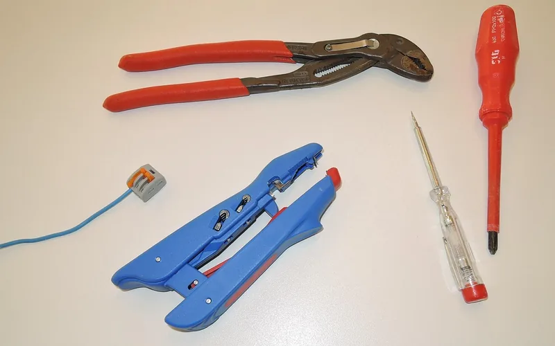 Electrician's voltage tester, wire strippers, and screwdrivers laid out for a repair