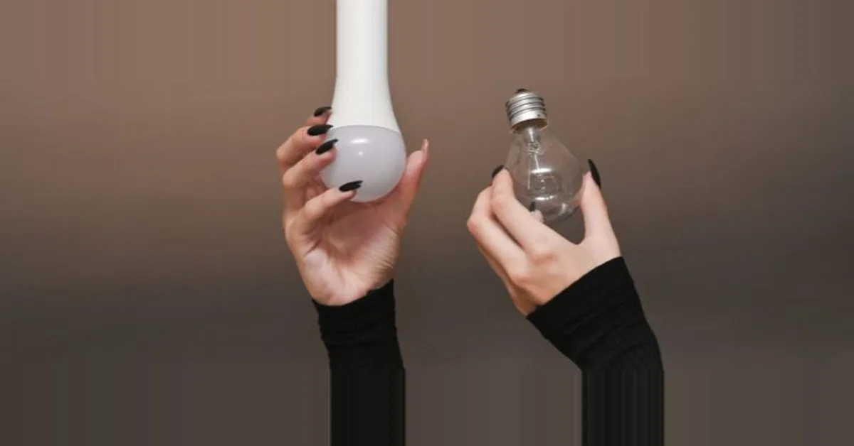 Hand holding a new LED light bulb beside the old incandescent bulb it replaces