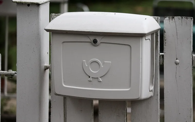 A white mailbox with a lock mounted on a fence post