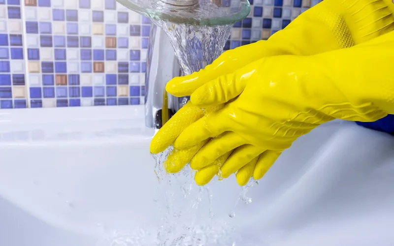 wearing yellow rubber gloves and washing hands at a bathroom sink wearing yellow rubber gloves and washing hands at a bathroom sink