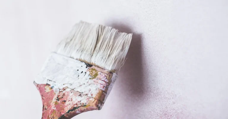 paintbrush applying white primer to a wall in even strokes