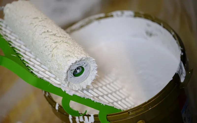 paint roller loaded with white primer resting on an open primer can paint roller loaded with white primer resting on an open primer can