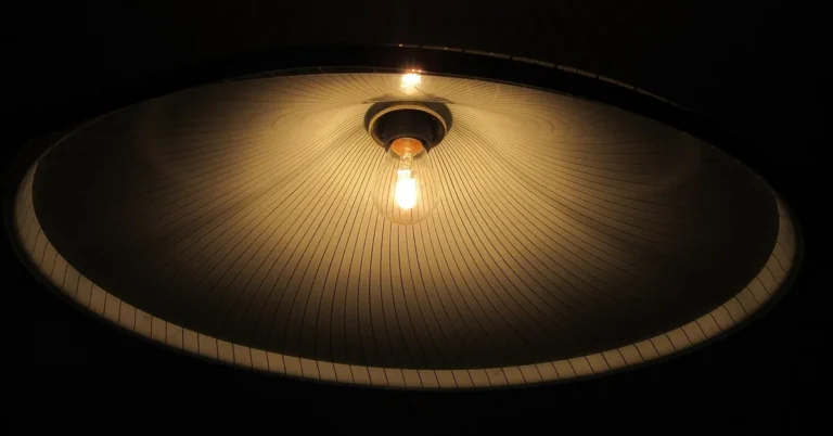 Warm light glowing through a pleated paper lampshade from an LED bulb below