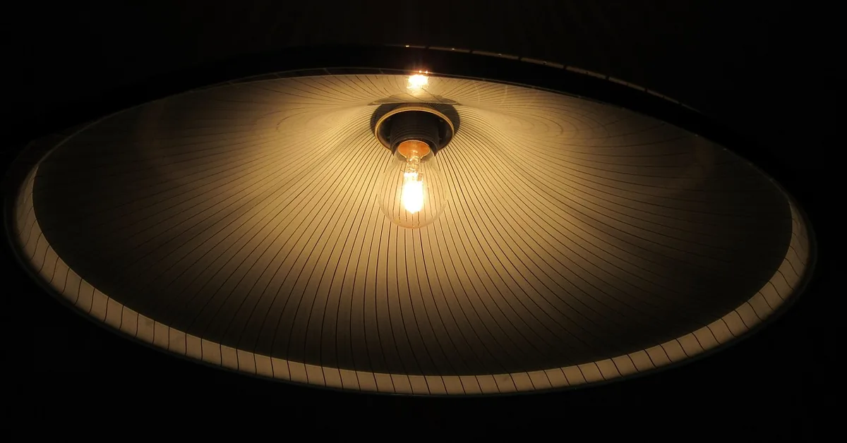 Warm light glowing through a pleated paper lampshade from an LED bulb below