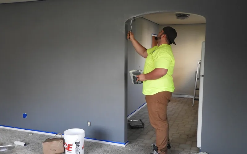 Painter rolling fresh gray paint onto an interior wall during a room renovation