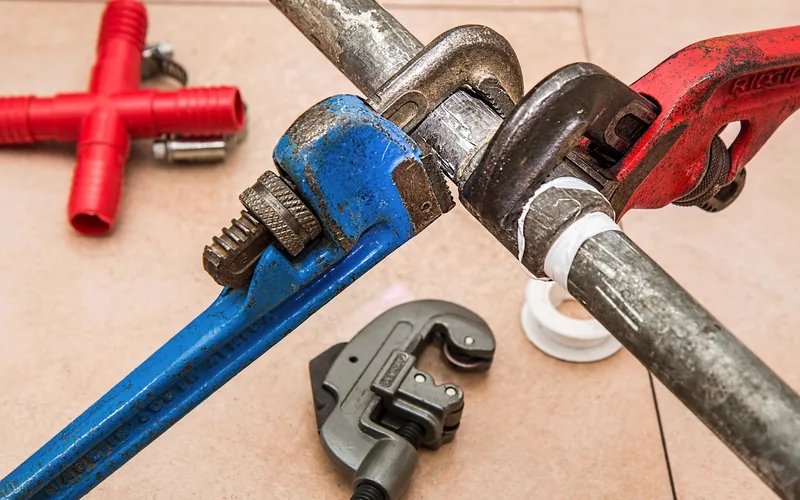 Pipe wrenches and plumbing tools laid out for a toilet tank repair job