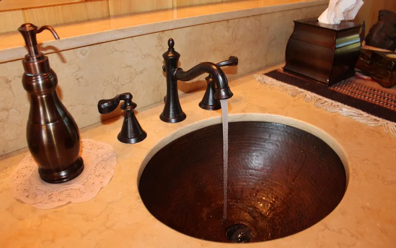 oil-rubbed bronze faucet being rinsed under running water after a vinegar soak