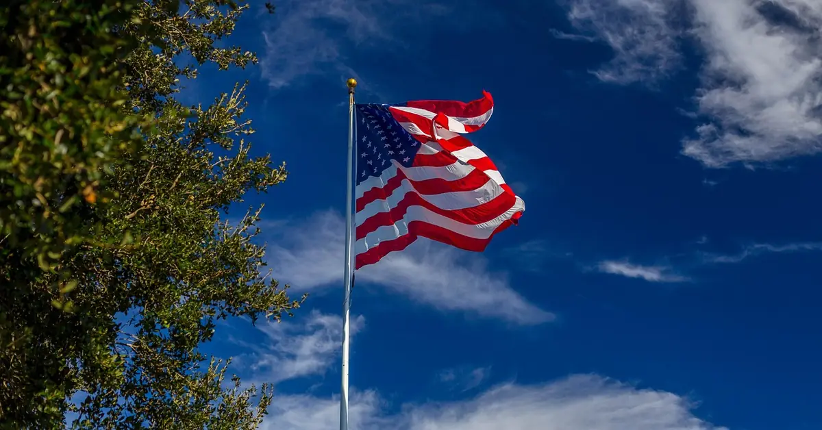 American flag flying on a wall-mounted pole against a clear blue sky