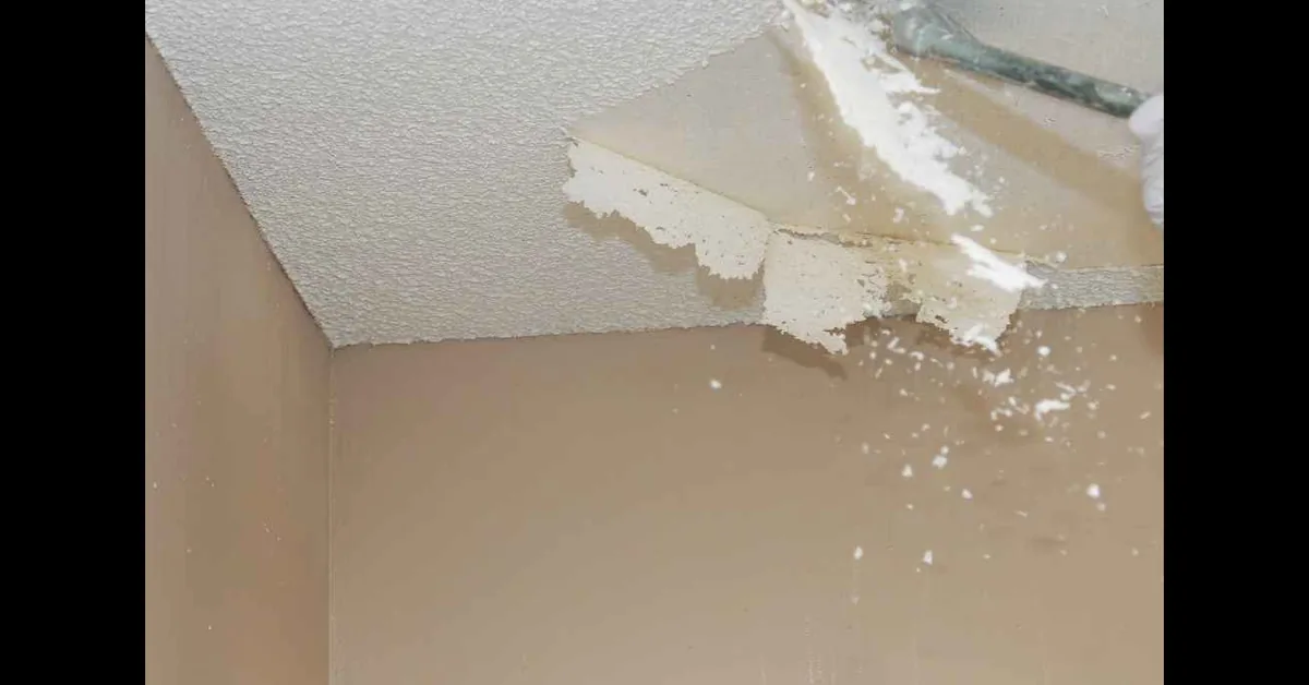 Putty knife scraping a section of painted popcorn ceiling texture down to the drywall