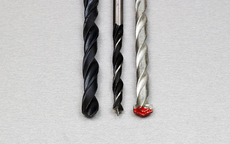 three drill bits compared including a masonry style bit with a red painted tip for hard materials