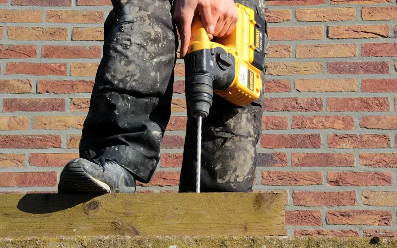 worker drilling a pilot hole through a pressure-treated board into a concrete ledge worker drilling a pilot hole through a pressure-treated board into a concrete ledge