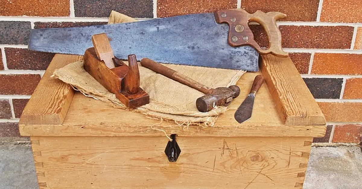 Hand saw and woodworking hand tools laid out on a wooden toolbox for mitre cuts