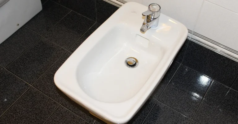 White ceramic bidet with chrome faucet in a modern tiled bathroom