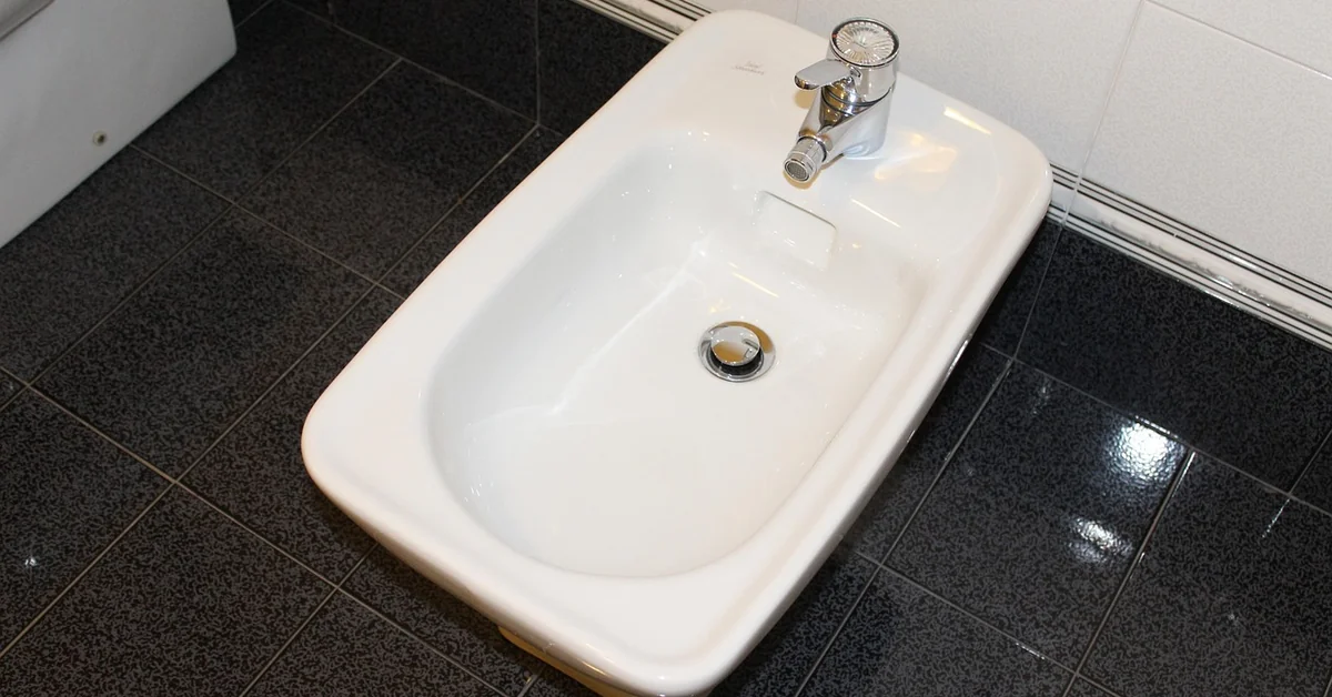 White ceramic bidet with chrome faucet in a modern tiled bathroom
